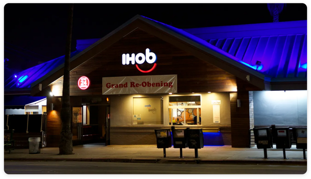Exterior of an IHOb restaurant at night with illuminated signage and a banner reading “Grand Re-Opening” above the entrance.